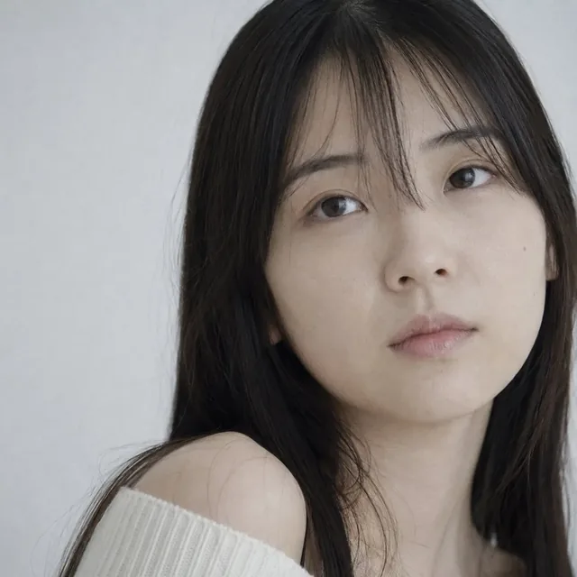 Extreme close-up portrait of a young Japanese woman's face, soft diffused daylight, subtle grain, pale skin, cream off-shoulder knit.