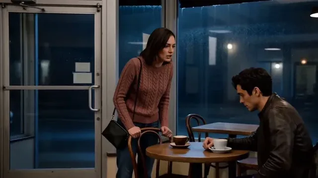 Two characters, Nora and Elias, have an intense argument in a small coffee shop during a rainy night. Nora is standing, visibly upset, while Elias is seated, looking downcast and ashamed.