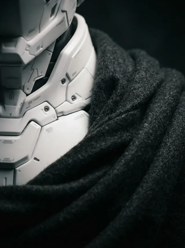Macro photograph of a white mecha suit collar against dark, folded wool drapery, with dramatic side lighting emphasizing textures and seams.