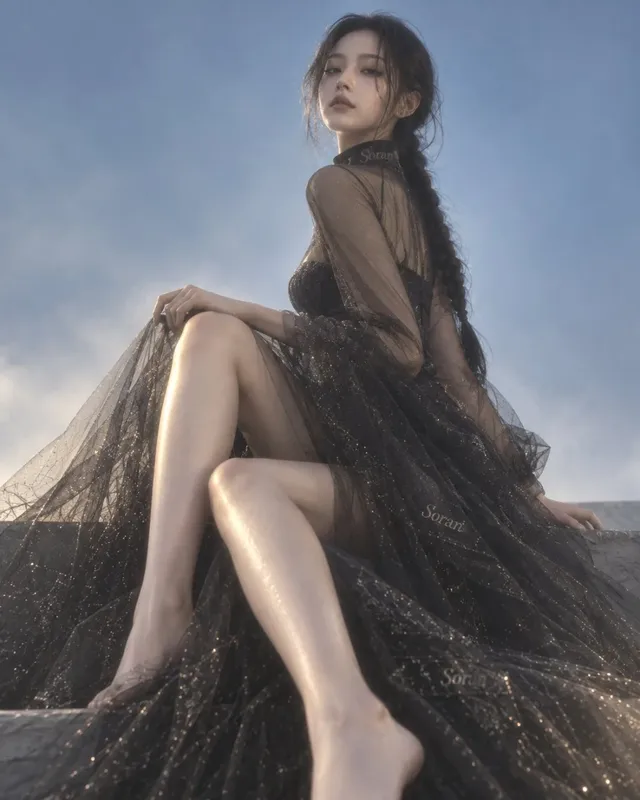 Low-angle wide shot of a tall, slender East Asian woman with fair skin, wearing a sheer black, flowing gown with subtle gold shimmer. She gazes down, creating a sense of distance and elegance against a minimalist background.