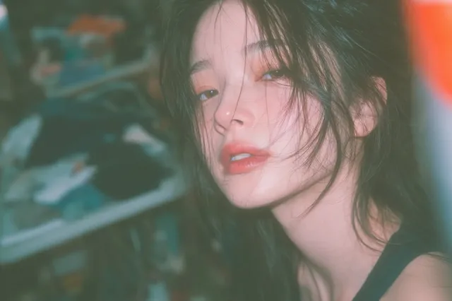 Off-center, half-face portrait of a seductive 20s Japanese woman with black-tea brown hair, in a laundromat, with a retro, bokeh-heavy, snapshot aesthetic.