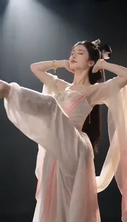 A young East Asian woman in a luxurious, flowing pink, white, and gold gradient Hanfu with intricate golden embroidery and a sheer, shimmering shawl, performing a dynamic and graceful dance sequence.