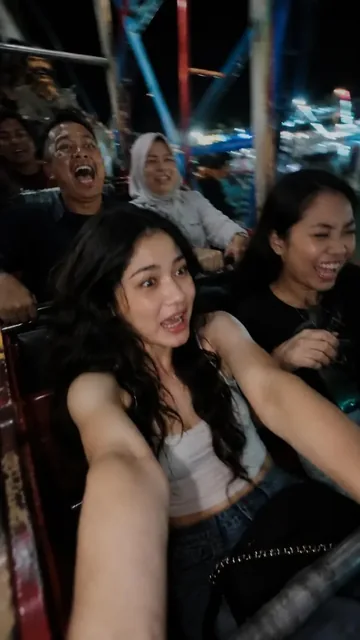A candid, ultra-realistic selfie taken at night on a fast amusement park ride, showing a person with wide eyes and open mouth in excitement, with motion blur and colorful carnival
