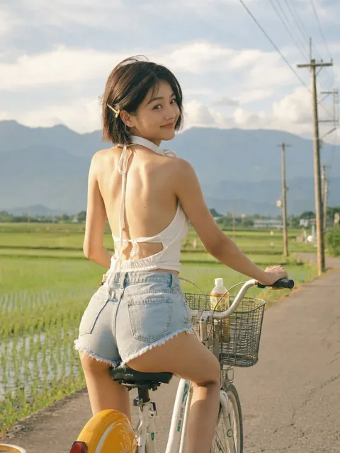 A young East Asian woman with a bob haircut rides a white city bicycle through a Taiwanese countryside road, looking back with a smile. She wears a white halter top and denim short