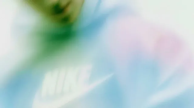 A blurred image of a person wearing a Nike hoodie with pastel green, blue, and pink hues.