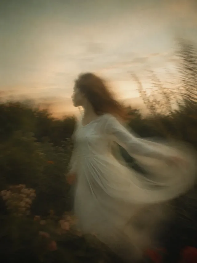A woman in a flowing white dress running through a natural landscape, her hair and dress blurred by motion, creating a sense of wind and movement.