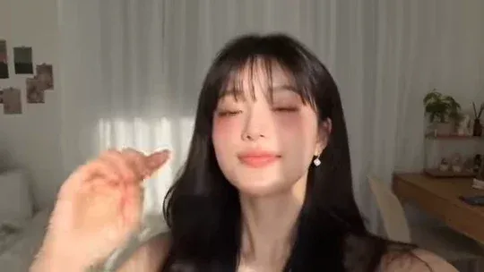 Young Japanese idol filming a personal vlog in her cozy bedroom, smiling softly at the camera with her cat nearby. The style is warm and nostalgic, like a digital diary.