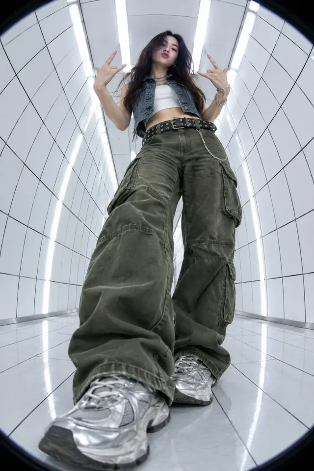 Extreme low-angle fisheye photograph of a young woman in Y2K street style, making rock hand gestures in a futuristic white grid tunnel with overhead lights.